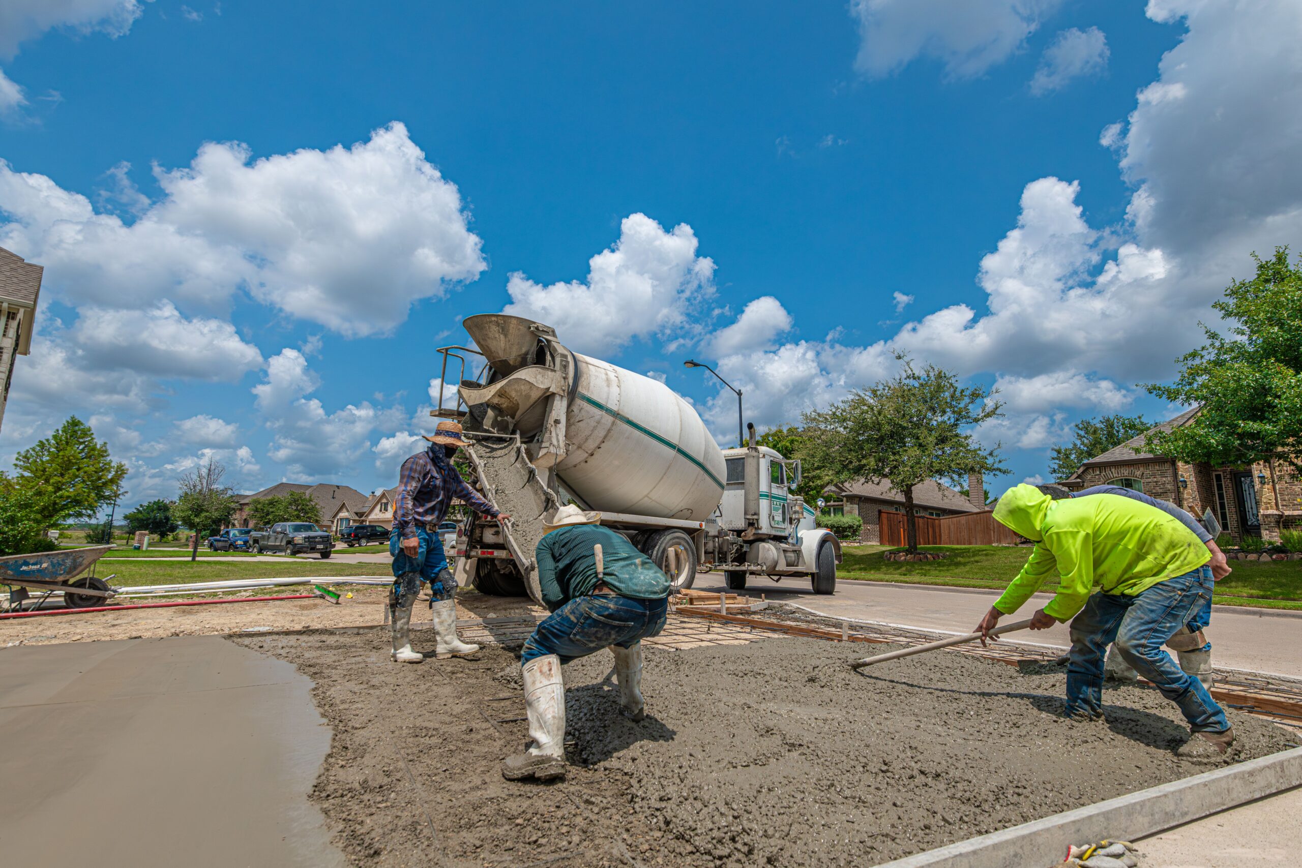 Construction workers laying concrete for a driveway in Fort Worth, Texas, under a bright blue sky.