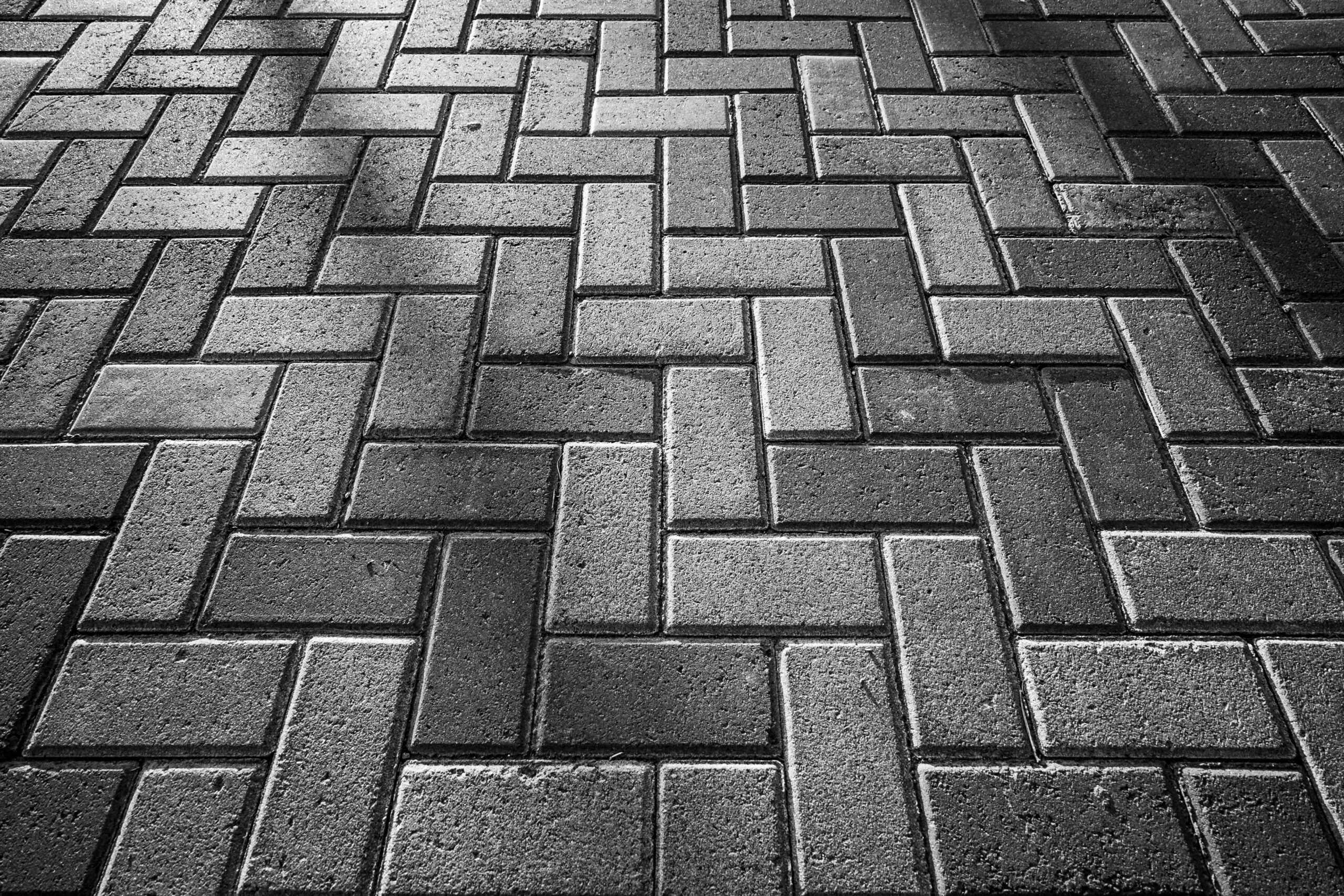 Monochrome image of brick pavement in herringbone pattern creating texture.