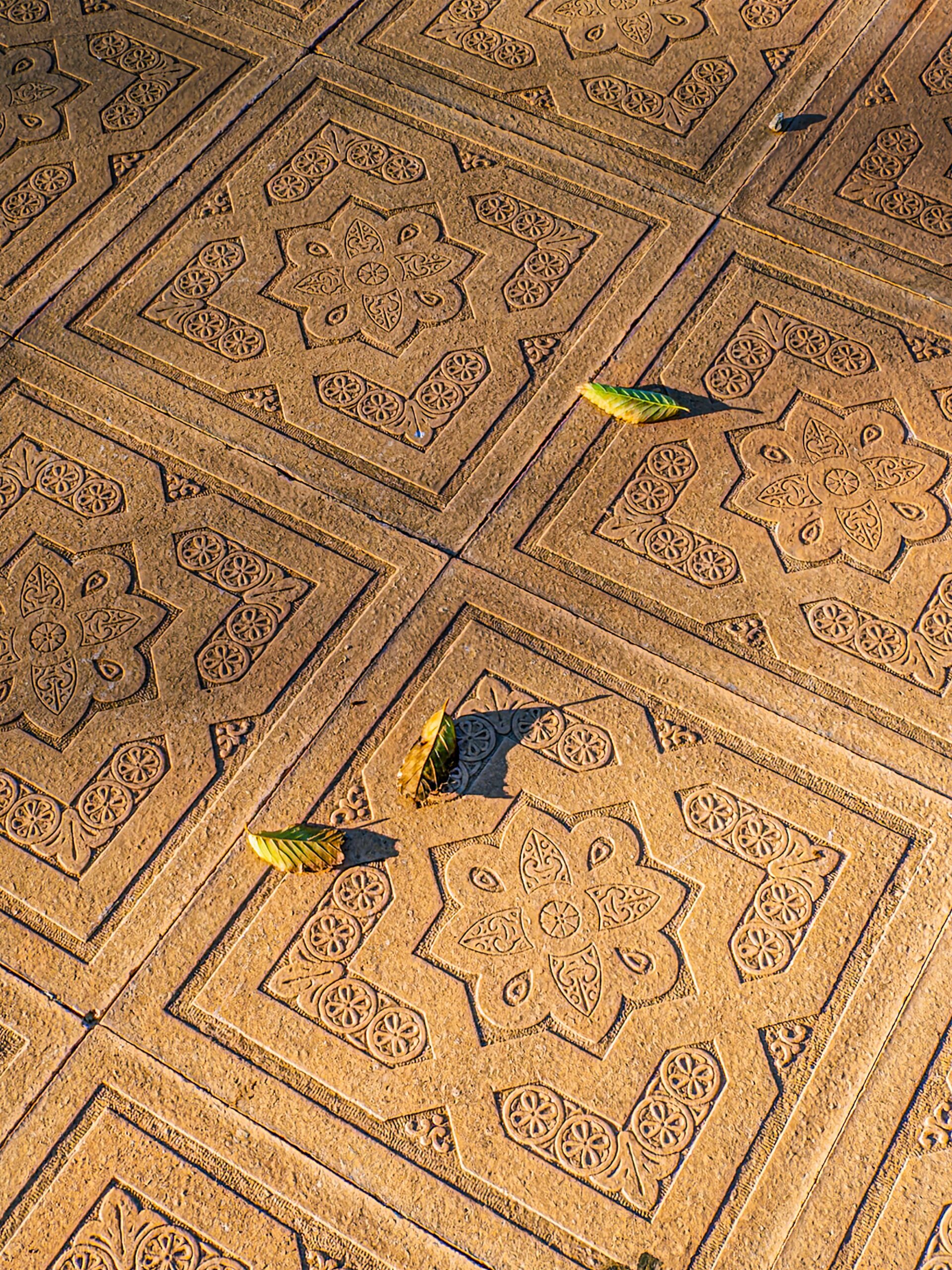 Detailed cobblestone design with leaf shadows in warm sunset light.